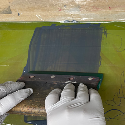 Silk screen squeegee being pulled across a screen to imprint an image on acrylic.